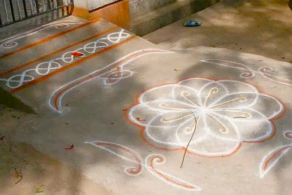 In Kodaikanal’s Palani Hills, Tamil Nadu, South India, locals create traditional intricate white and orange rangoli floral patterns on doorsteps during festivals to welcome prosperity.