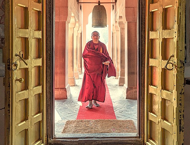 A Buddhist monk's deep relationship with his faith is evident as he walks through a temple at the Sarnath UNESCO site near Varanasi, India, framed by golden doors.