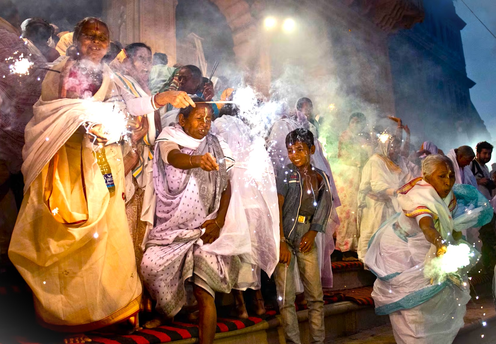 Colorful festival on Lake Pichola in Udaipur, Rajasthan, India, features elderly women in traditional attire celebrating with fireworks aboard a Shikara boat tour under palace arches, capturing vibrant cultural spirit. Colorful festival on Lake Pichola in Udaipur, Rajasthan, India, features elderly women in traditional attire celebrating with fireworks aboard a Shikara boat tour under palace arches, capturing vibrant cultural spirit.
