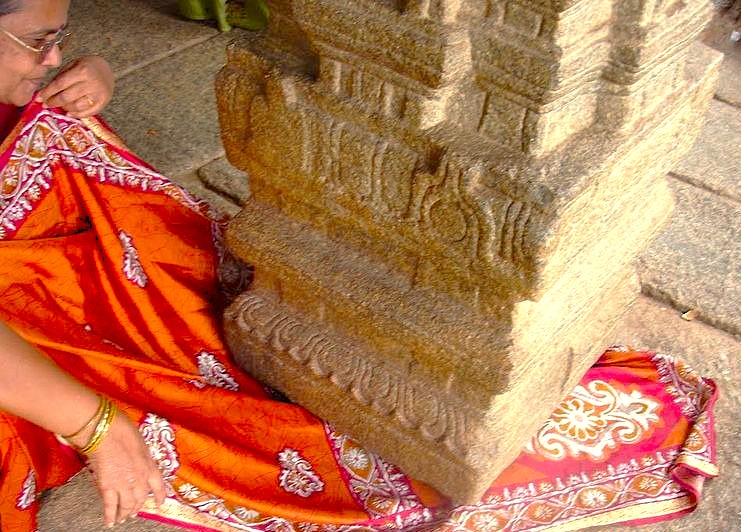 A woman passes her sari under the famous floating pillar at the Lepakshi Temple in Andhra Pradesh, India, an architectural marvel located near the giant Jatayu Sculpture attraction.