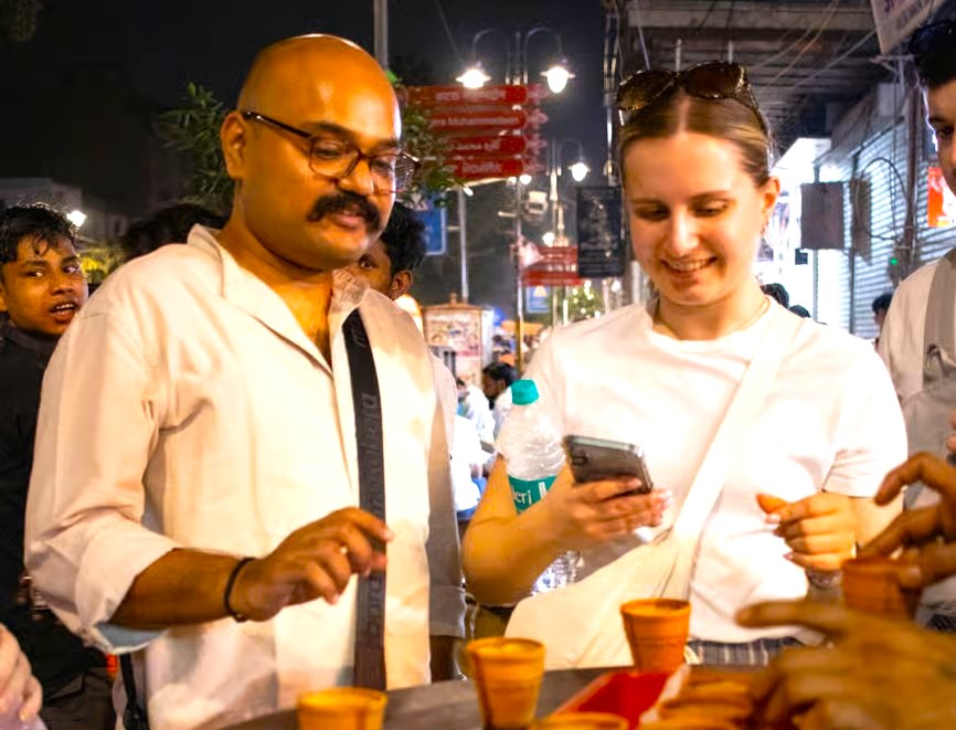 A local guide and a tourist enjoy street chai, a classic experience during the Madurai to Munnar road trip in Tamil Nadu, India, a journey through the scenic UNESCO Western Ghats.