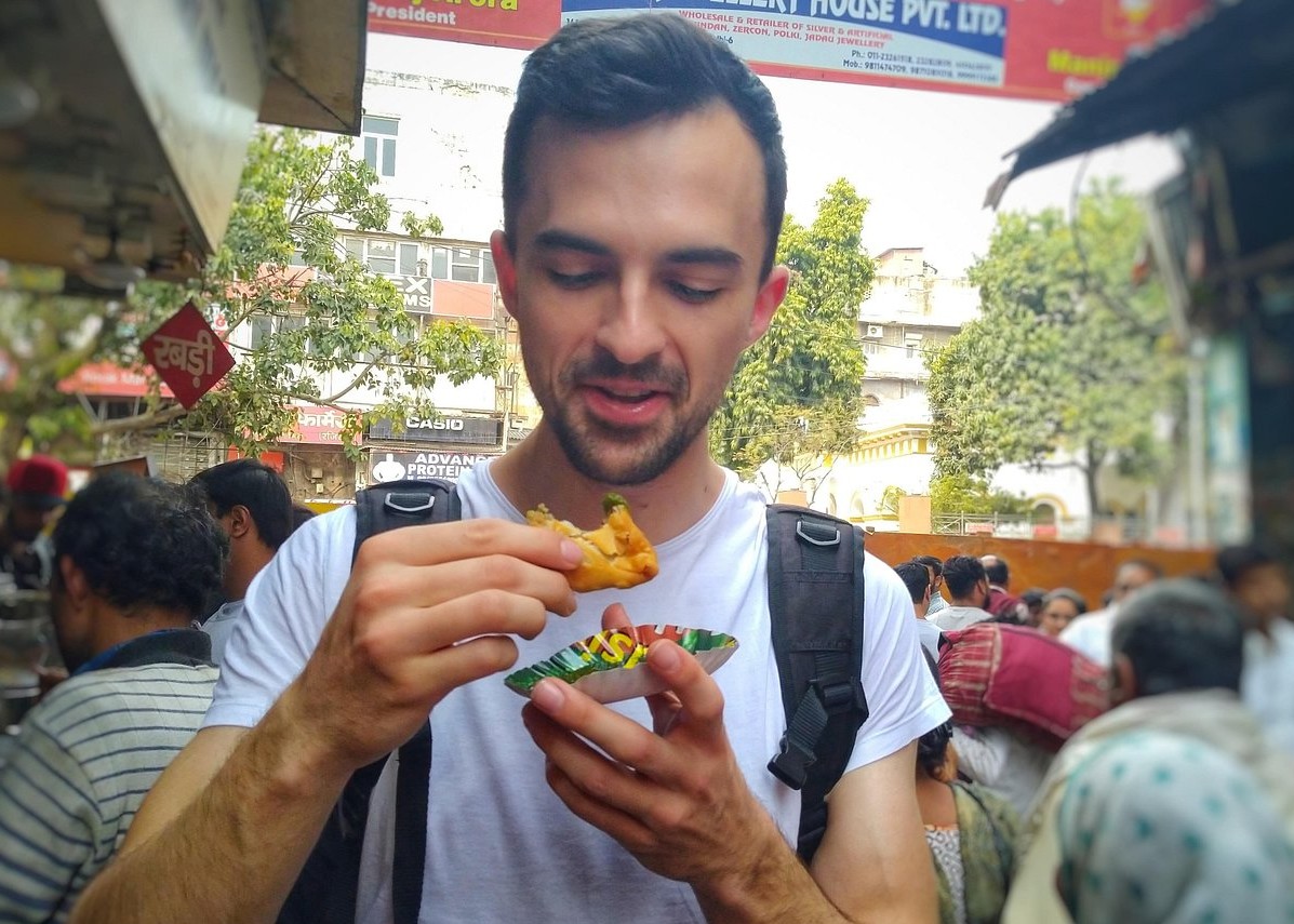 Smiling tourist sampling crispy street pakora from a bustling roadside stall in a vibrant South India market, set against Tamil Nadu’s urban backdrop Madurai.