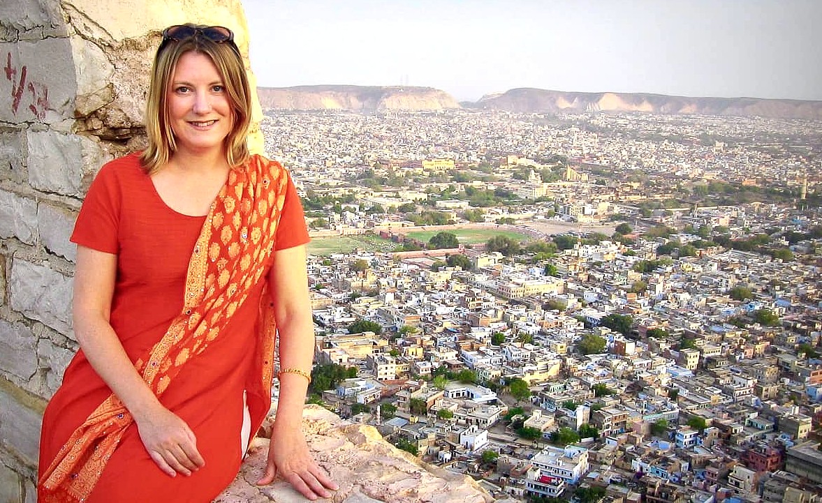 “Woman seated on historic stone rampart overlooking Mathura skyline in Uttar Pradesh, India, embodies cultural heritage, travel inspiration, scenic cityscape, vibrant attire, unforgettable tour experience.” “Woman seated on historic stone rampart overlooking Mathura skyline in Uttar Pradesh, India, embodies cultural heritage, travel inspiration, scenic cityscape, vibrant attire, unforgettable tour experience.”