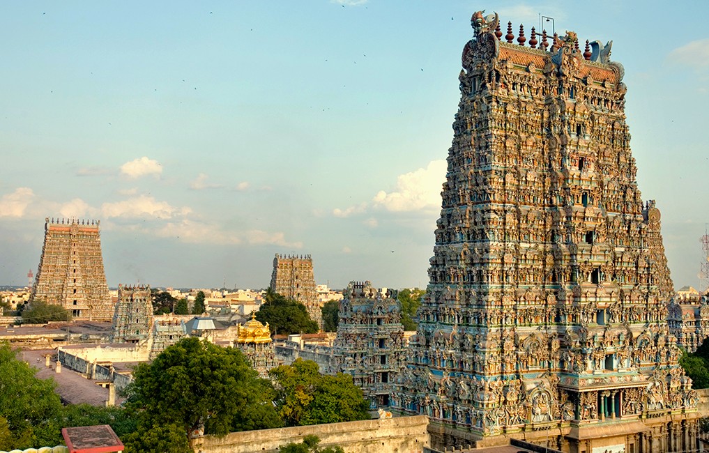 An expansive panorama of the ornate majestic Dravidian gopurams and vibrant sculptures of Meenakshi Temple rising above lush greenery against a radiant sky in historic Madurai, Tamil Nadu, South India. An expansive panorama of the ornate majestic Dravidian gopurams and vibrant sculptures of Meenakshi Temple rising above lush greenery against a radiant sky in historic Madurai, Tamil Nadu, South India.