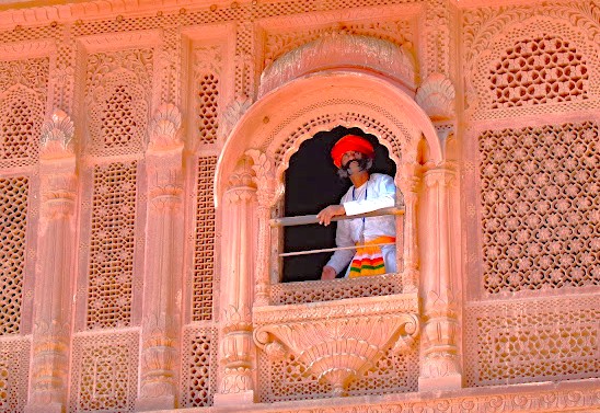 Traditional Rajasthani man in vibrant turban and embroidered kurta stands at ornate sandstone jharokha overlooking iconic Mehrangarh Fort courtyard, Jodhpur, Rajasthan, India, highlighting cultural heritage, architectural detail and tourism appeal. Traditional Rajasthani man in vibrant turban and embroidered kurta stands at ornate sandstone jharokha overlooking iconic Mehrangarh Fort courtyard, Jodhpur, Rajasthan, India, highlighting cultural heritage, architectural detail and tourism appeal.