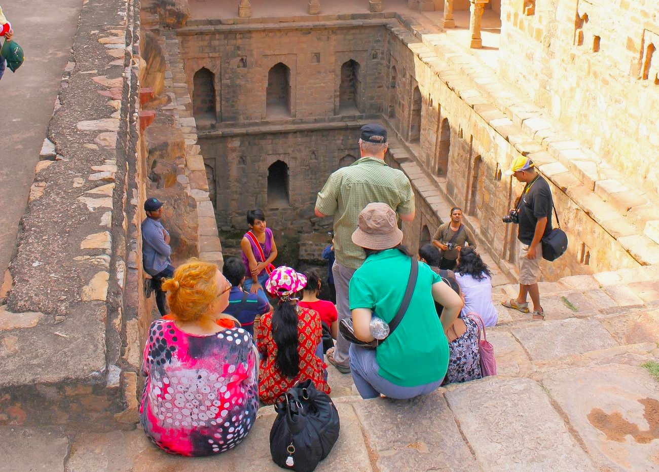 A diverse group of tourists sits on the ancient stone steps of Rajon Ki Baoli stepwell inside Mehrauli Archaeological Park in Delhi, India, during a guided tour showcasing historical architecture. A diverse group of tourists sits on the ancient stone steps of Rajon Ki Baoli stepwell inside Mehrauli Archaeological Park in Delhi, India, during a guided tour showcasing historical architecture.