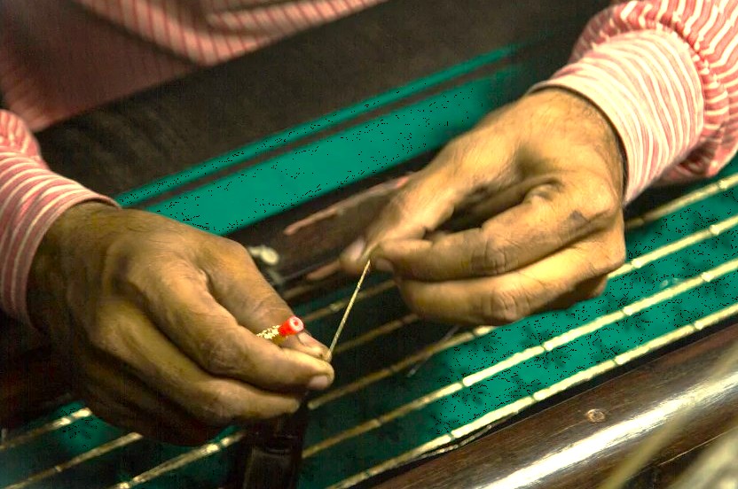 An artisan at Mehrotra-silks in Varanasi, India, shows the detailed relationship with their craft, carefully preparing golden thread for weaving near the historic Sarnath UNESCO site.