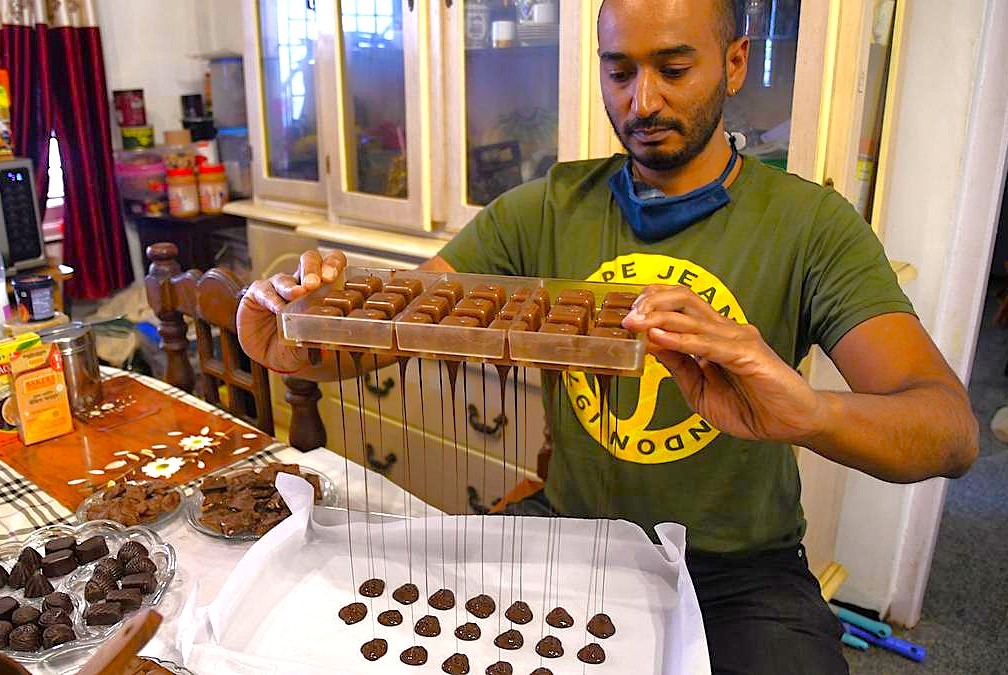 Moddy’s Chocolate artisan in Ooty, Tamil Nadu, Southern India drips handcrafted chocolate confections using traditional hanging method in a cozy kitchen workshop, highlighting artisanal craftsmanship. Moddy’s Chocolate artisan in Ooty, Tamil Nadu, Southern India drips handcrafted chocolate confections using traditional hanging method in a cozy kitchen workshop, highlighting artisanal craftsmanship.