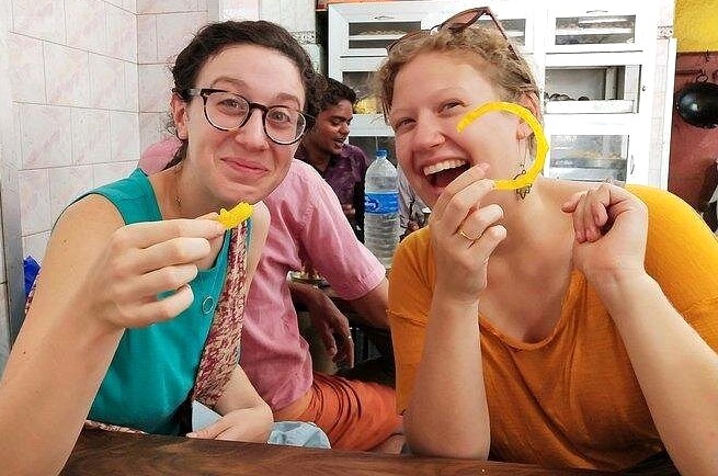 Two friends share a local Mumbai street snack at a cozy café in Mahapradesh, India, smiling broadly as they bond, savoring flavors, capturing casual travel moments, cultural immersion, warm hospitality. Two friends share a local Mumbai street snack at a cozy café in Mahapradesh, India, smiling broadly as they bond, savoring flavors, capturing casual travel moments, cultural immersion, warm hospitality.