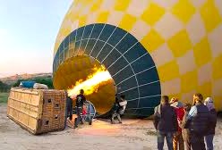 Colorful hot air balloon inflates at dawn over lush fields, offering scenic Mysore hot air ballooning experiences in Karnataka, India, with pilots guiding passengers aloft.