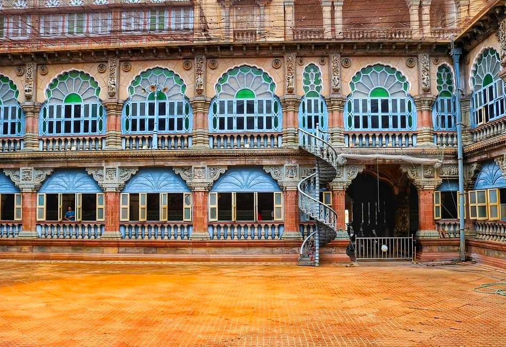 Spiral staircase courtyard of Mysore Palace in Karnataka, India features ornate arches, carved stone balconies, colorful tiled flooring, historic facade, royal cultural heritage landmark grandeur.