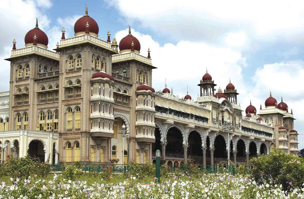 “Mysore Palace in Karnataka, India showcases stunning Indo-Saracenic architecture with ornate red onion domes, arches, intricate carvings, lush gardens and rich cultural heritage, royal landmark.”