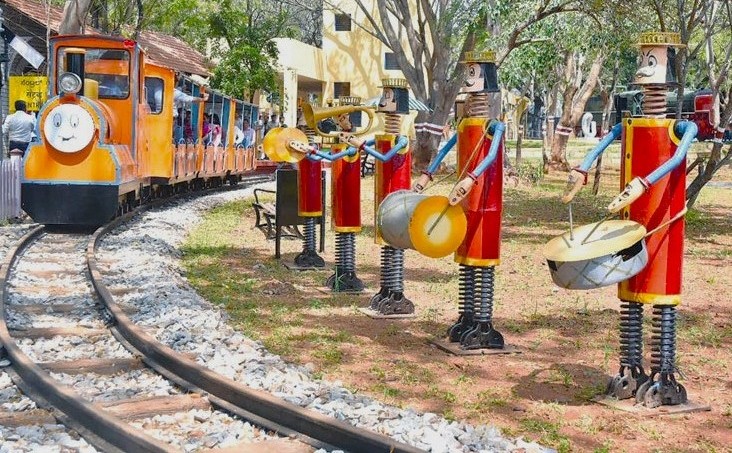 Colorful cartoon train ride winding through grassy park with whimsical soldier musicians at India Railway Museum in Mysore, Karnataka, India, offering family fun and heritage. Colorful cartoon train ride winding through grassy park with whimsical soldier musicians at India Railway Museum in Mysore, Karnataka, India, offering family fun and heritage.