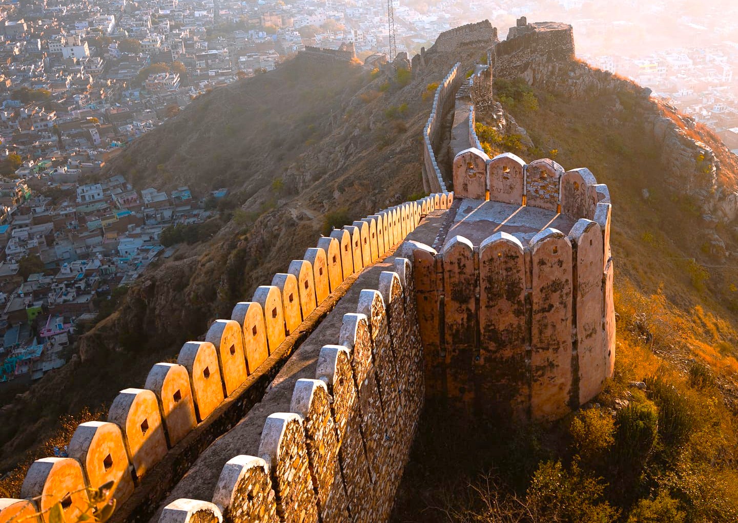 Spectacular panoramic view of Nahargarh Fort’s sandstone battlements atop the Aravalli hills overlooking Jaipur’s pink city skyline at sunset in Rajasthan, India, showcasing historic hilltop architecture and cultural heritage tourism.