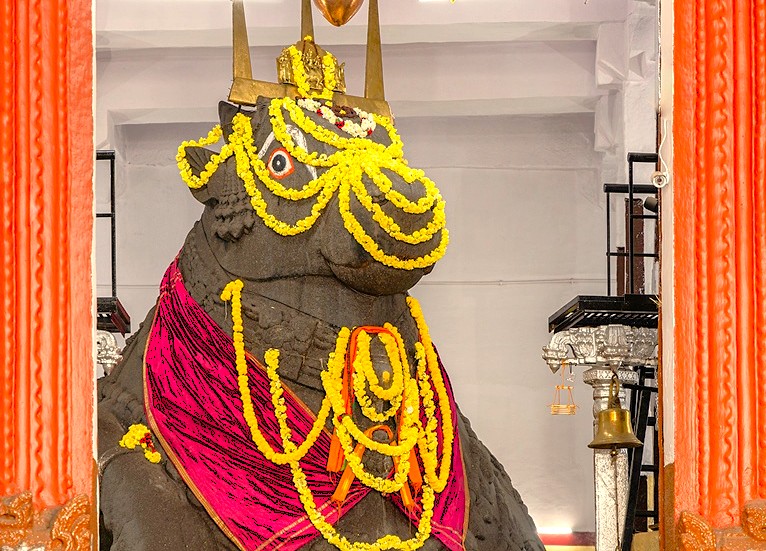 Intricately carved Nandi Bull Temple in Bangalore, Karnataka, India, near Mysore Palace, showcasing a majestic bull statue adorned with colorful flower garlands, nestled amid lush greenery, offering serene spiritual ambiance. Intricately carved Nandi Bull Temple in Bangalore, Karnataka, India, near Mysore Palace, showcasing a majestic bull statue adorned with colorful flower garlands, nestled amid lush greenery, offering serene spiritual ambiance.