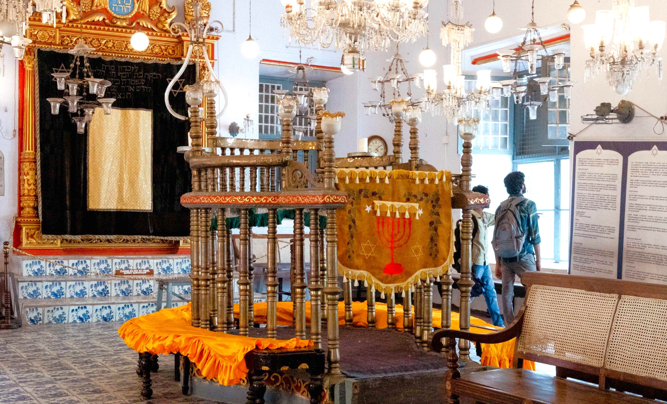 Discover the ornate wooden bimah and embroidered Torah ark curtain framed by sparkling chandeliers and ceramic tiles inside Paradesi Synagogue Kochi, a historic Jewish heritage site in South India’s Kerala. Discover the ornate wooden bimah and embroidered Torah ark curtain framed by sparkling chandeliers and ceramic tiles inside Paradesi Synagogue Kochi, a historic Jewish heritage site in South India’s Kerala.