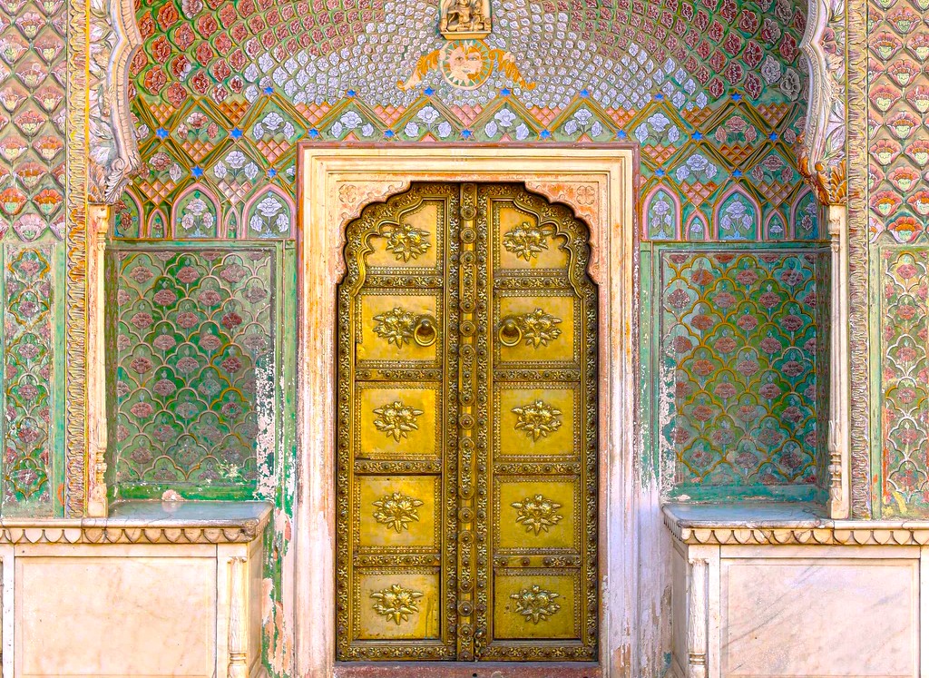 An intricately carved golden doorway set within vibrant teal and rose mosaic arches at Patrika Gate, Jaipur, Rajasthan, India, exemplifies Mughal-inspired architectural artistry, cultural heritage, ornate craftsmanship, and historic preservation.
