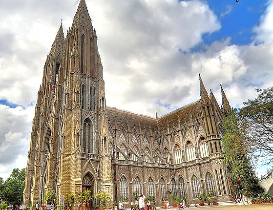 Gothic spired facade of Saint Philomena’s Church in Mysore, Karnataka, India features twin towers, pointed arches, stained-glass windows, intricate stone carvings, peaceful historic religious landmark.