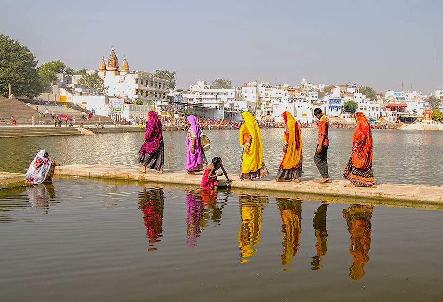 Women in vibrant saris cross a walkway along the Pushkar Lake ghats in Rajasthan, India, situated between Jaipur and Agra on the route to the Taj Mahal, reflecting local life.