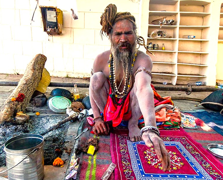 Ascetic Hindu sadhu with ritual items sitting on colorful rug performs devotional rites in Pushkar, Rajasthan, India, between Jaipur and Agra en route to the Taj Mahal, reflecting spiritual tradition.
