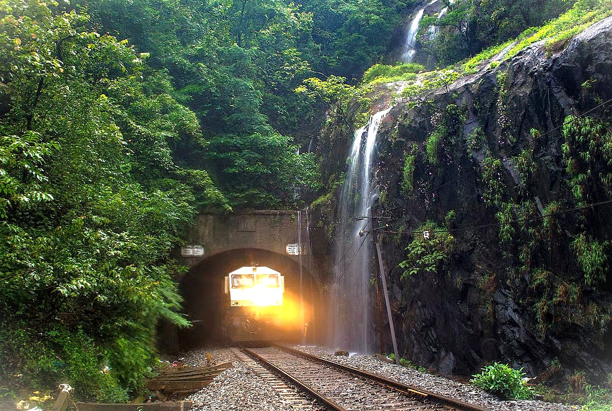 A train exits a tunnel by a waterfall on the scenic Goa to Mumbai railway trip in India, a famous journey in Maharashtra near UNESCO sites like the Elephanta Caves. A train exits a tunnel by a waterfall on the scenic Goa to Mumbai railway trip in India, a famous journey in Maharashtra near UNESCO sites like the Elephanta Caves.