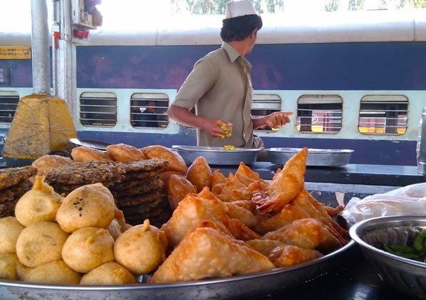 Colorful trays of kachori, samosas at an Indian railway platform stall in Rajasthan, welcoming travelers on their Railway Journey from Delhi to Bikaner into the Thar Desert with authentic snacks.