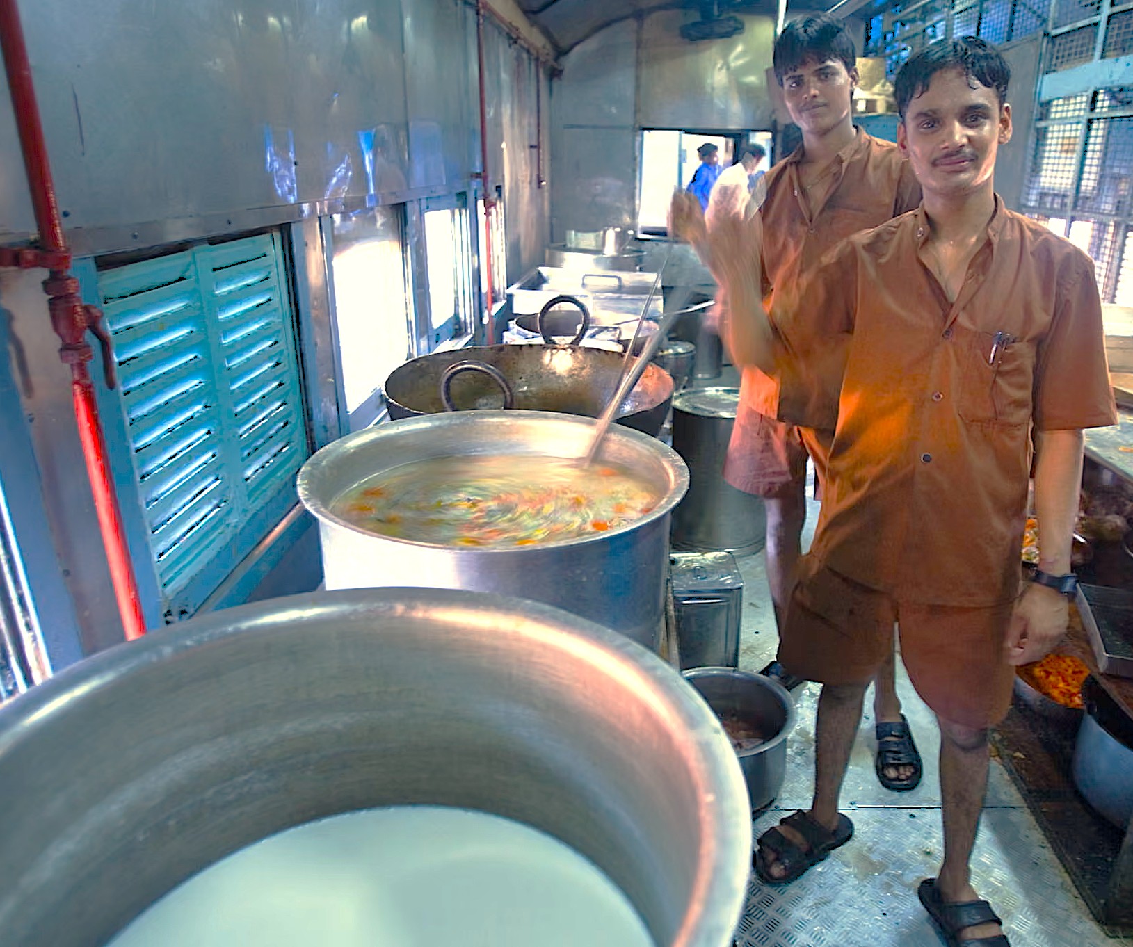 Two chefs in brown uniforms prepare steaming meals in a train kitchen in Mumbai, India, near iconic UNESCO-listed Elephanta Caves, enriching the Aurangabad railway journey to Elora and Ajanta Caves.