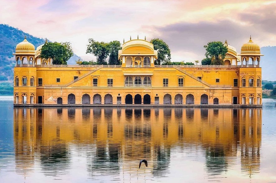 A serene Mughal-style yellow domed palace rising from calm lake waters at sunrise in Rajasthan, India, reflecting intricate waterfront architecture and picturesque, tranquil natural surroundings. A serene Mughal-style yellow domed palace rising from calm lake waters at sunrise in Rajasthan, India, reflecting intricate waterfront architecture and picturesque, tranquil natural surroundings.