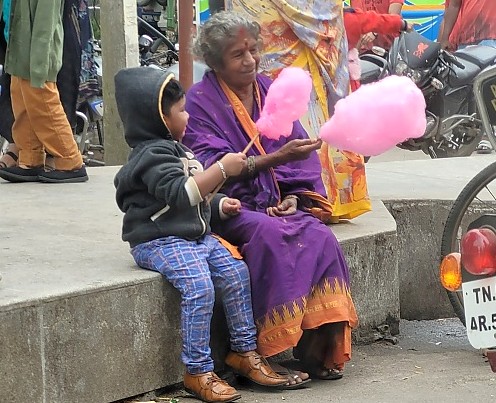 Road trip from Coimbatore to Kodaikanal, Tamil Nadu, India, enchants travelers with roadside treats like cotton candy shared between grandmother and child against bustling backdrop. Road trip from Coimbatore to Kodaikanal, Tamil Nadu, India, enchants travelers with roadside treats like cotton candy shared between grandmother and child against bustling backdrop.