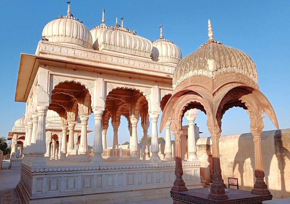 White marble Royal Cenotaphs at Devikund Sagar in Bikaner, Rajasthan, India stand against clear blue skies near the Thar Desert, showcasing intricate carvings, domed pavilions and a regal cultural heritage landmark. White marble Royal Cenotaphs at Devikund Sagar in Bikaner, Rajasthan, India stand against clear blue skies near the Thar Desert, showcasing intricate carvings, domed pavilions and a regal cultural heritage landmark.