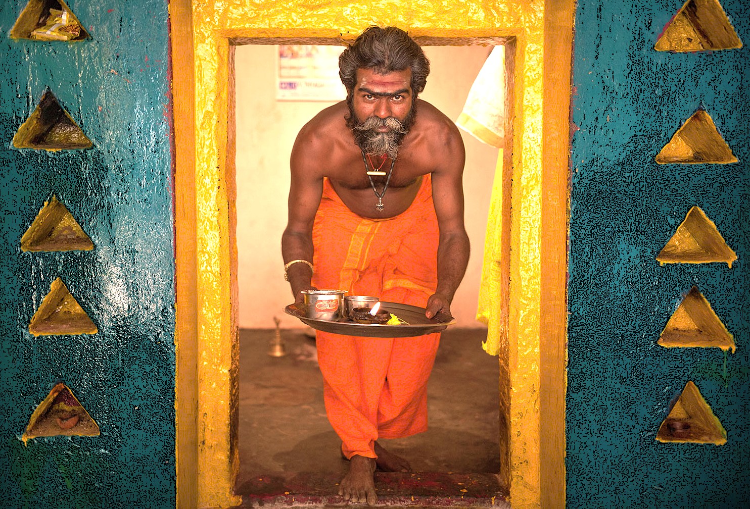 A striking portrait of a Sadhu holding a puja offering tray at a local shrine in Badami, Karnataka, India, embodies the deep spiritual heritage found in this historic town, located near the magnificent Pattadakal UNESCO World Heritage site.