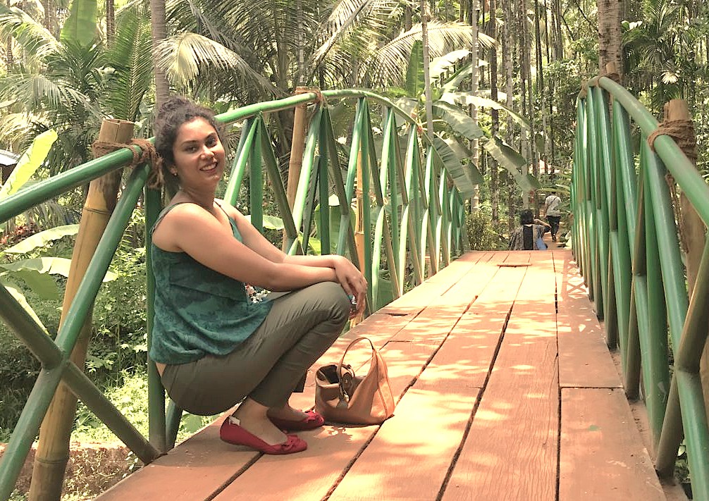 A tourist poses on a bridge at a plantation, a popular eco-tour in Goa, India, often combined with visiting beaches or Old Goa Unesco churches like Se Cathedral.