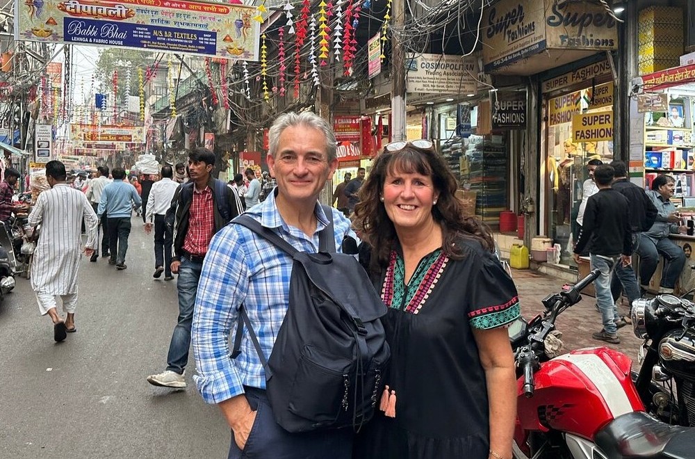 A couple exploring the bustling marketplace in Mysore, Karnataka, at India’s Sea Shell Museum, vibrant street stalls with local textiles, motorcycles, and festive decorations overhead.