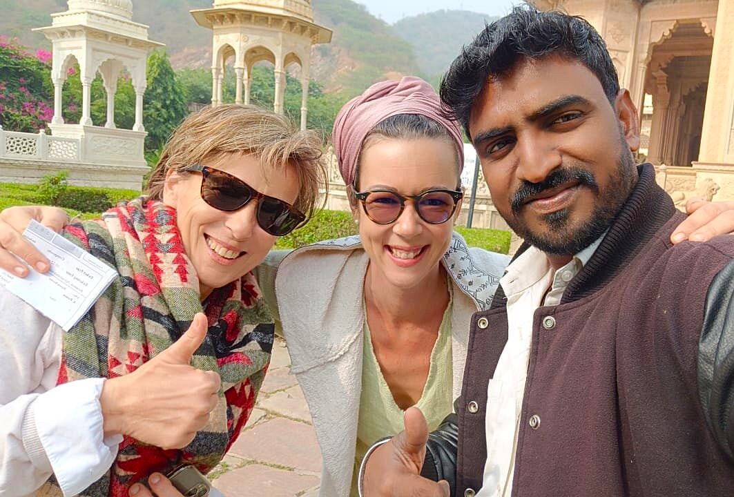 Three smiling travelers capture a joyful selfie outside the UNESCO-listed Sheesh Mahal in Jaipur, Rajasthan, India, surrounded by ornate pavilions and lush gardens, reflecting the palace’s vibrant heritage and architecture.