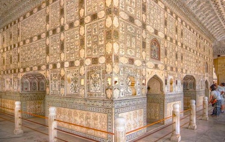 Opulent sunlit mirrored walls and intricate pietra dura patterns at Sheesh Mahal, Jaipur, Rajasthan, India, showcase royal Mughal artistry and UNESCO heritage status, captivating visitors exploring the historic palace interior.