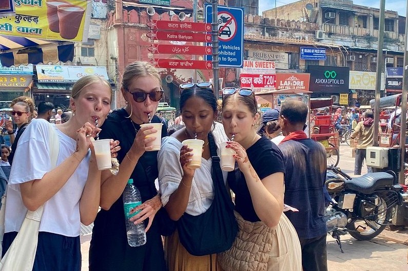Four tourists savor traditional filter coffee at a bustling street market near Srirangapatna Fort, Mysore, Karnataka, India, capturing vibrant culture, local flavors, and festive ambiance.