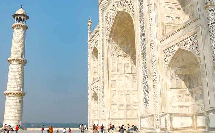 Visitors admire the intricately carved marble facade and soaring minaret of the Taj Mahal in Agra, Uttar Pradesh, India, set against a blue sky in a UNESCO World Heritage courtyard. Visitors admire the intricately carved marble facade and soaring minaret of the Taj Mahal in Agra, Uttar Pradesh, India, set against a blue sky in a UNESCO World Heritage courtyard.