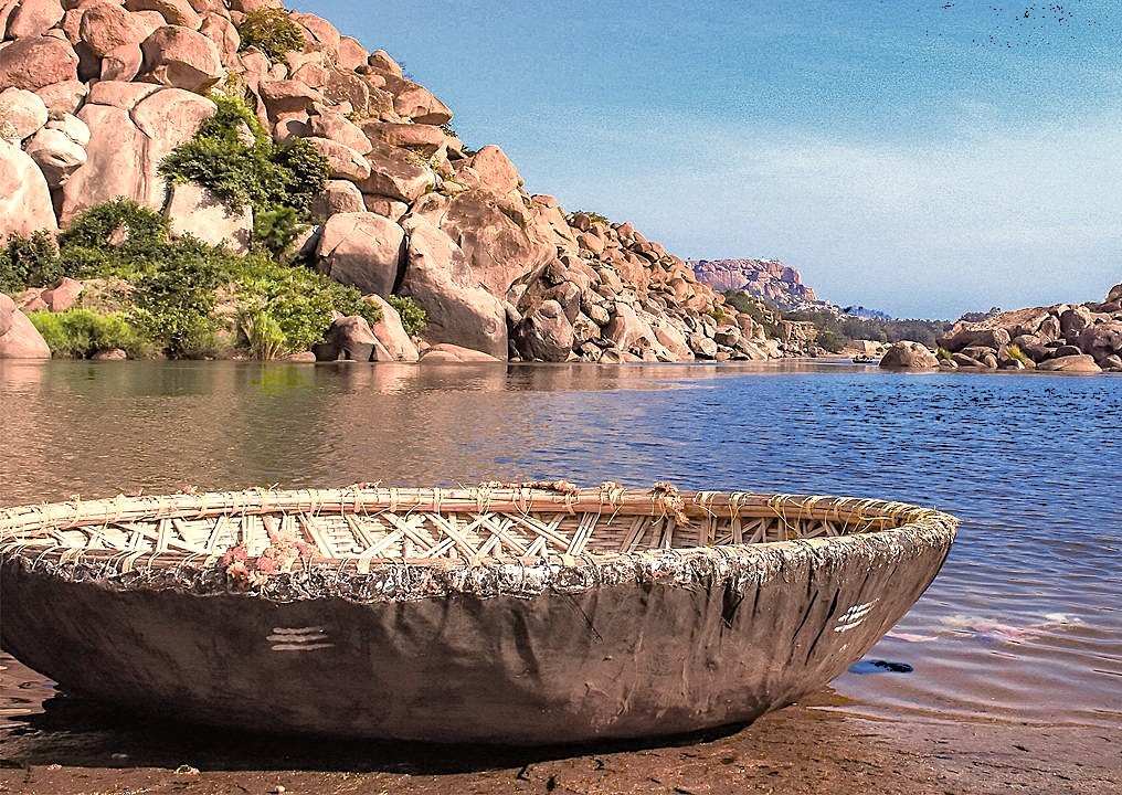 A traditional coracle boat on the Tungabhadra River in Hampi Karnataka, India, offering a unique way to explore the boulder landscapes surrounding the region's famous ancient Unesco sites.