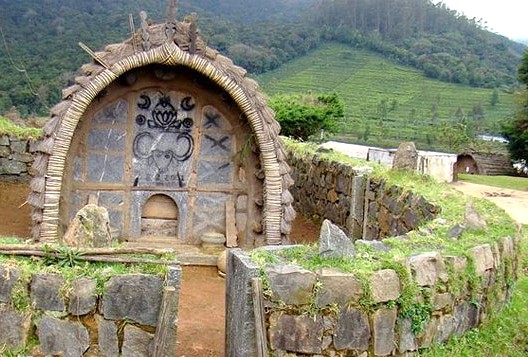 Rustic Toda hut shrine carved in stone set against lush green hills in Ooty, Tamil Nadu, southern India, reflecting tribal architecture, cultural heritage, scenic landscape.