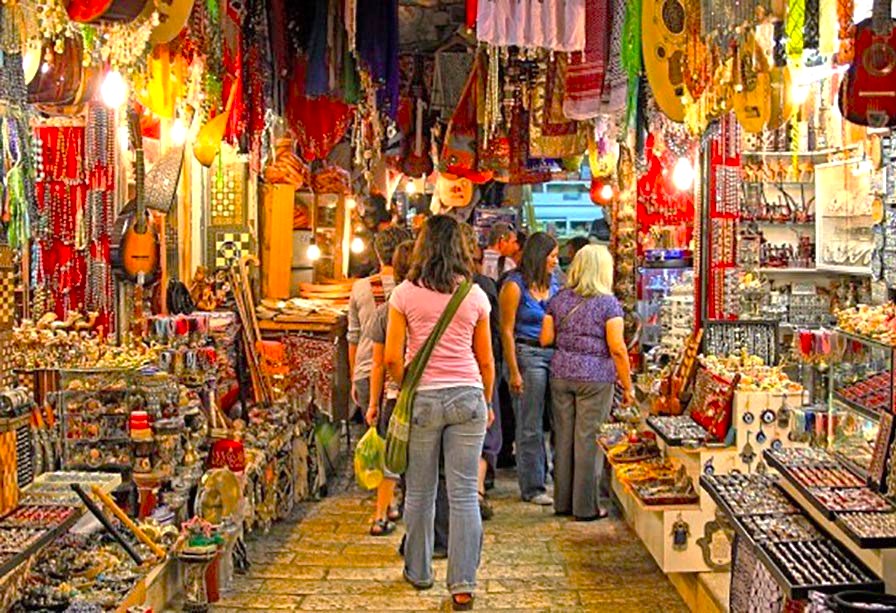 Tourists browsing colorful handicrafts and jewelry stalls in Udaipur’s vibrant market near Ahar Cenotaphs, Rajasthan, India, featuring traditional Rajasthani souvenirs, textiles, musical instruments, lively outdoor bazaar atmosphere, local artisans’ creations.