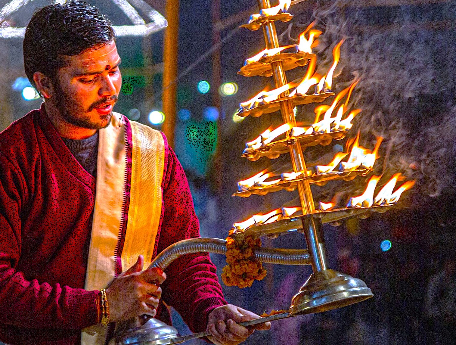 Young priest performing sacred Ganga Aarti ceremony at Dasaswamedh Ghat in Varanasi, India, near the Sarnath UNESCO site, illuminating the riverfront with vibrant spiritual traditional Hindu flame ritual at dusk.