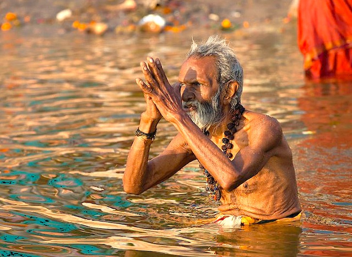 Elderly Hindu ascetic performs morning ritual prayer in the sacred Ganges River at Varanasi, Uttar Pradesh, India, near Sarnath Temple Buddha and Bharat Kala Bhavan Museum, wearing colorful prayer beads