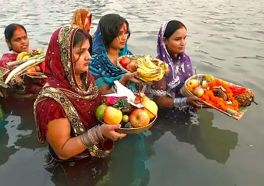 Women in colorful saris offer fruits, flowers, and prayers into the Ganges near the Sanarth Temple and Buddha shrine in Varanasi, Uttar Pradesh, India, during a sacred river worship festival.