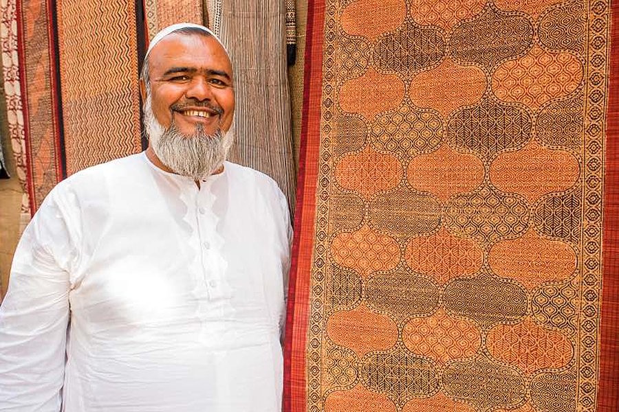 Smiling artisan in white kurta showcases intricately woven block-printed textiles at a craft fair in the Western Ghats of southern India, celebrating traditional heritage craftsmanship.